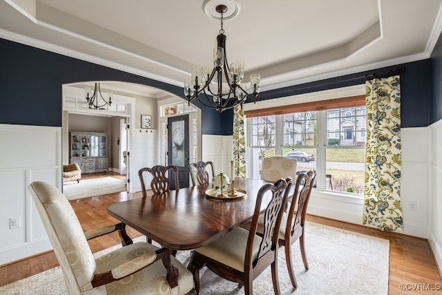 dining space with a raised ceiling, a wainscoted wall, a notable chandelier, and light wood-style flooring