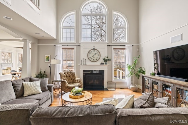 living area featuring ornate columns, a fireplace with flush hearth, a high ceiling, and wood finished floors