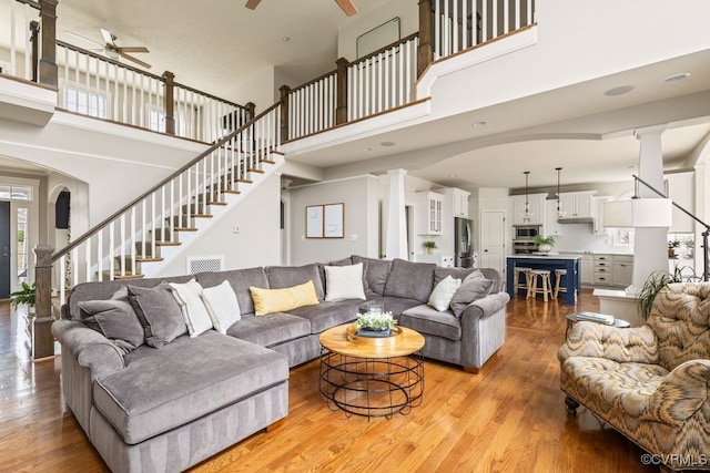 living room featuring a ceiling fan, light wood-style flooring, stairway, and ornate columns