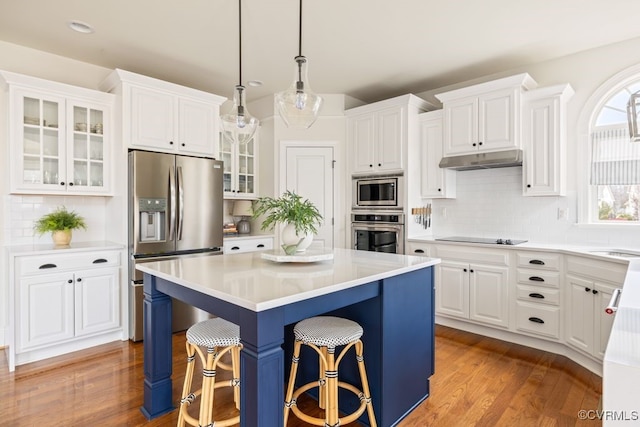 kitchen with under cabinet range hood, stainless steel appliances, a kitchen island, white cabinetry, and a kitchen bar