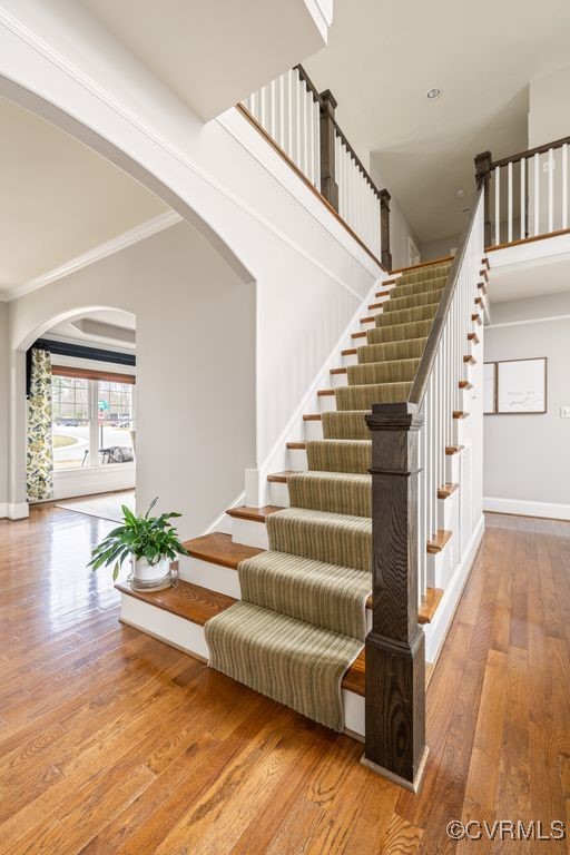 stairway featuring arched walkways, hardwood / wood-style floors, ornamental molding, and baseboards