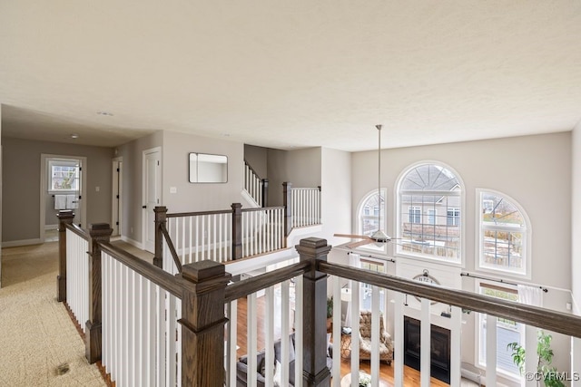 hallway with an upstairs landing, baseboards, and light colored carpet