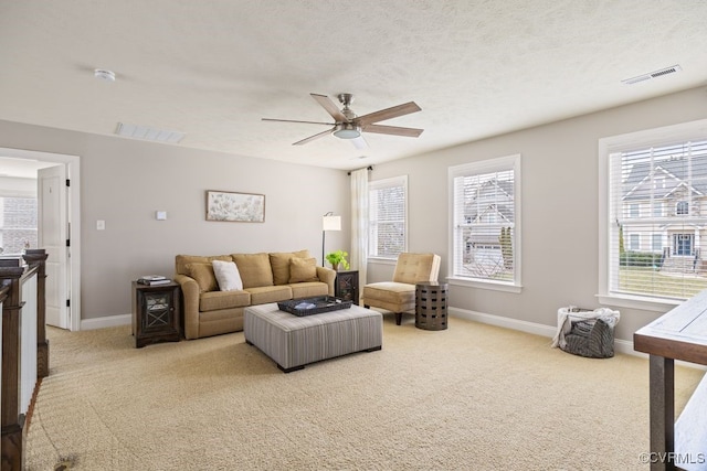 carpeted living area with a ceiling fan, visible vents, a textured ceiling, and baseboards