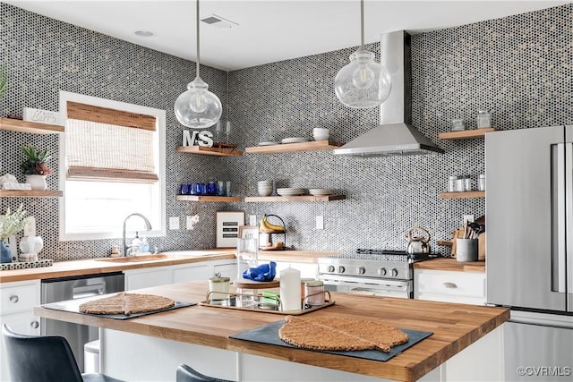 kitchen featuring wall chimney range hood, wood counters, appliances with stainless steel finishes, and open shelves