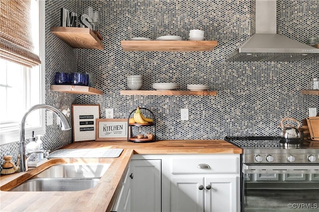 kitchen with wall chimney range hood, butcher block countertops, open shelves, and a sink