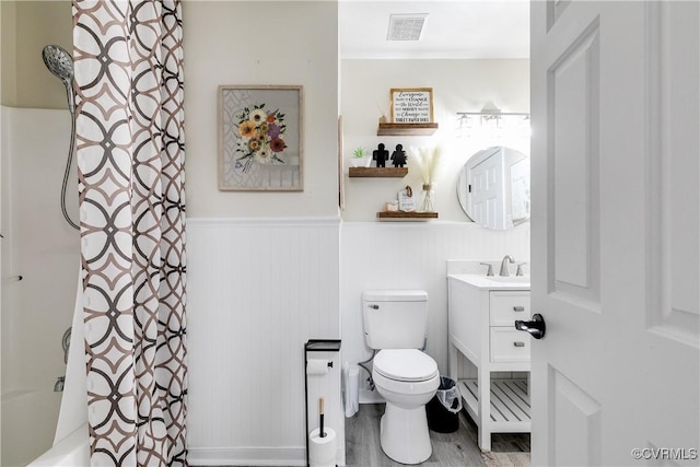 bathroom with visible vents, toilet, a wainscoted wall, shower / bath combination with curtain, and vanity