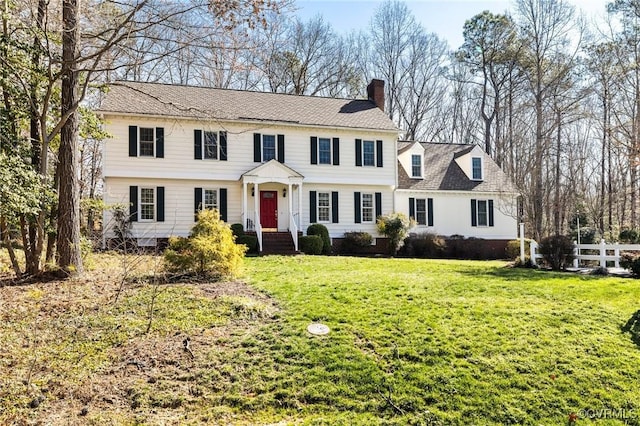 colonial inspired home with a chimney, a front yard, and fence