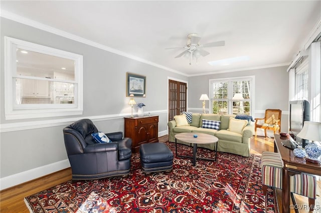 living area featuring a ceiling fan, baseboards, crown molding, and wood finished floors