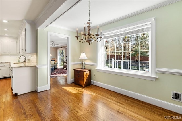 unfurnished dining area with wood finished floors, a sink, visible vents, baseboards, and ornamental molding