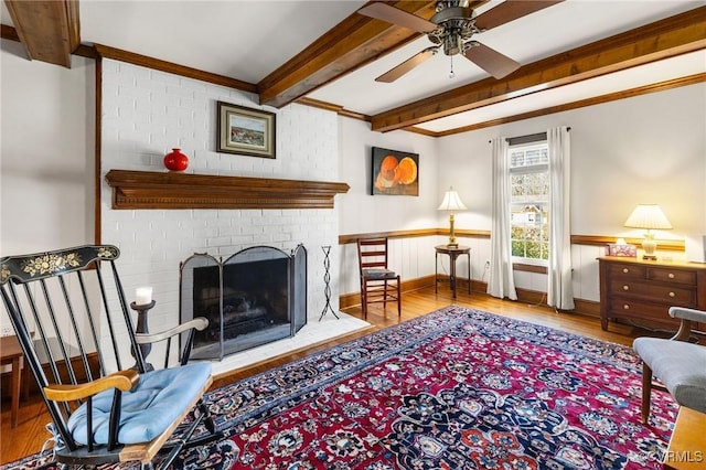 living area with ornamental molding, beamed ceiling, a brick fireplace, and wood finished floors