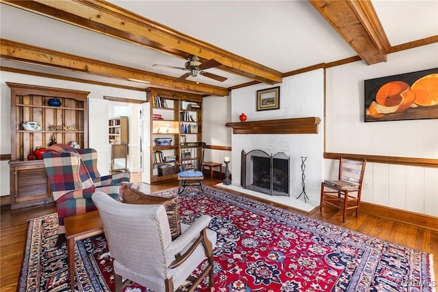 living room featuring a fireplace, wood finished floors, a ceiling fan, baseboards, and beamed ceiling