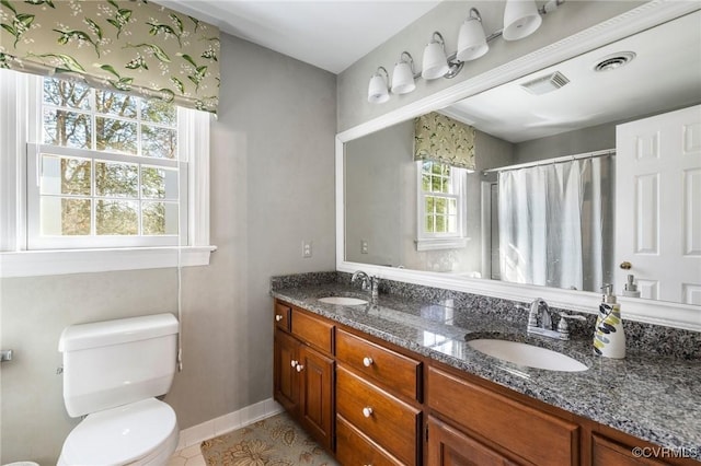 bathroom with toilet, double vanity, visible vents, and a sink