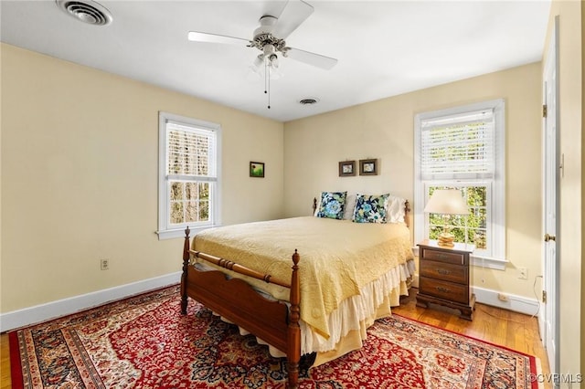 bedroom featuring a ceiling fan, wood finished floors, visible vents, and baseboards