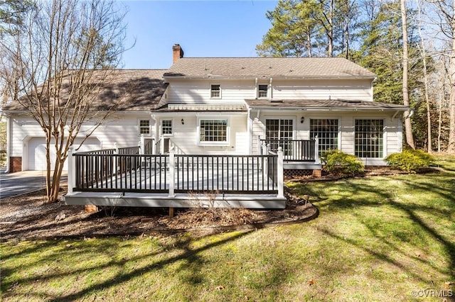 rear view of property with driveway, a chimney, an attached garage, a deck, and a yard