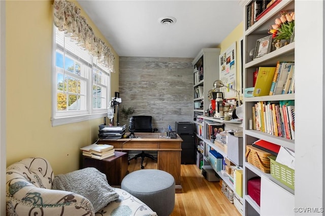 office featuring an accent wall, visible vents, wood walls, and wood finished floors