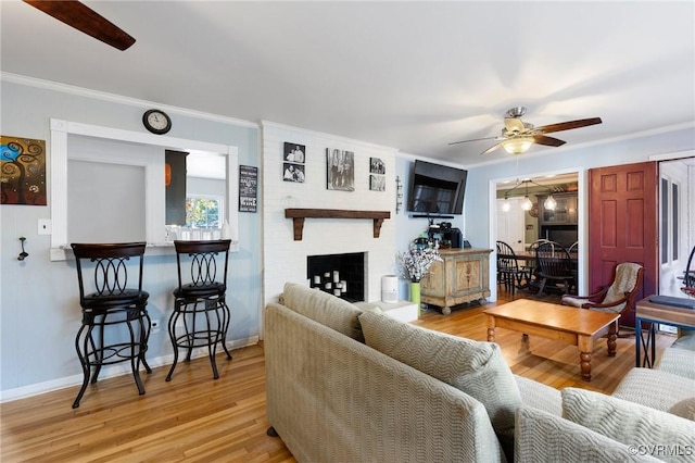 living room with a large fireplace, crown molding, a ceiling fan, and wood finished floors