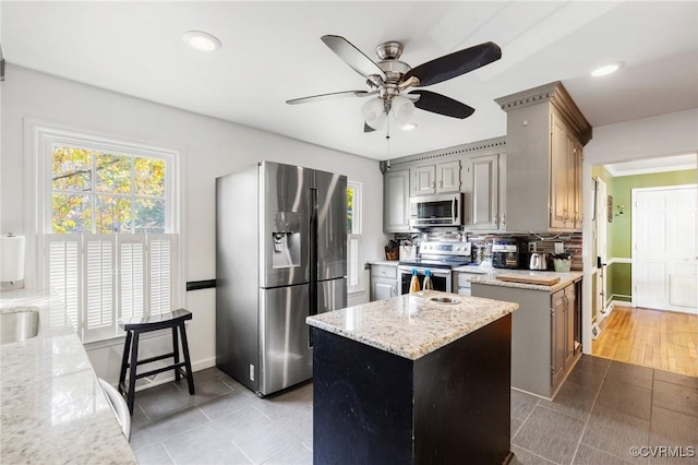 kitchen featuring recessed lighting, decorative backsplash, appliances with stainless steel finishes, a kitchen island, and light stone countertops