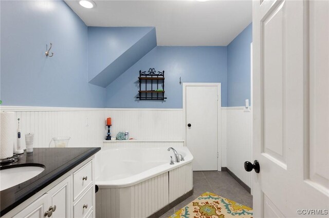 bathroom with a wainscoted wall, tile patterned floors, a garden tub, and vanity