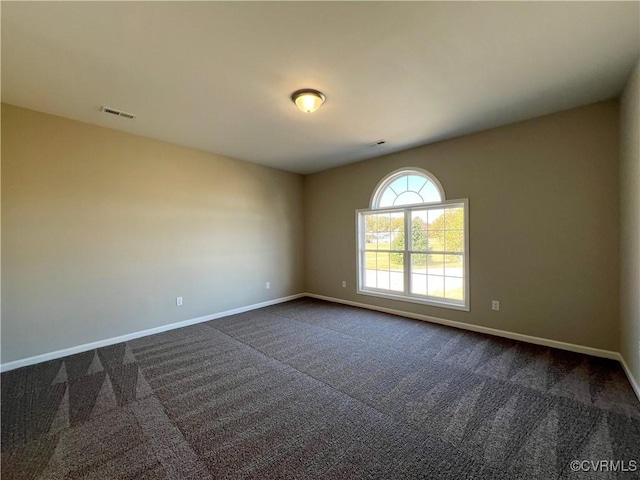 empty room with dark colored carpet, visible vents, and baseboards