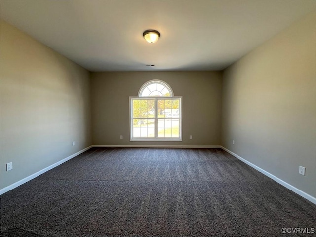 unfurnished room featuring dark colored carpet and baseboards