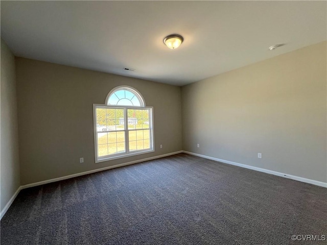 spare room featuring dark carpet, visible vents, and baseboards