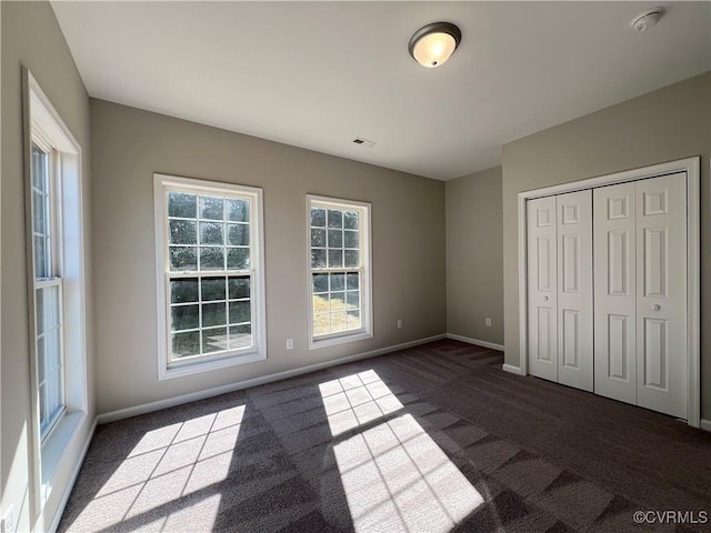 unfurnished bedroom featuring a closet, visible vents, dark carpet, and baseboards