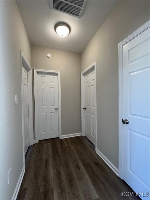 corridor with baseboards, visible vents, and dark wood-style flooring