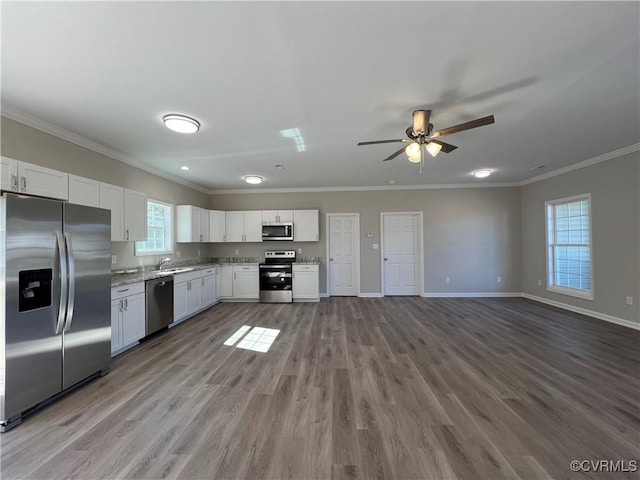 kitchen with appliances with stainless steel finishes, white cabinets, ornamental molding, and baseboards