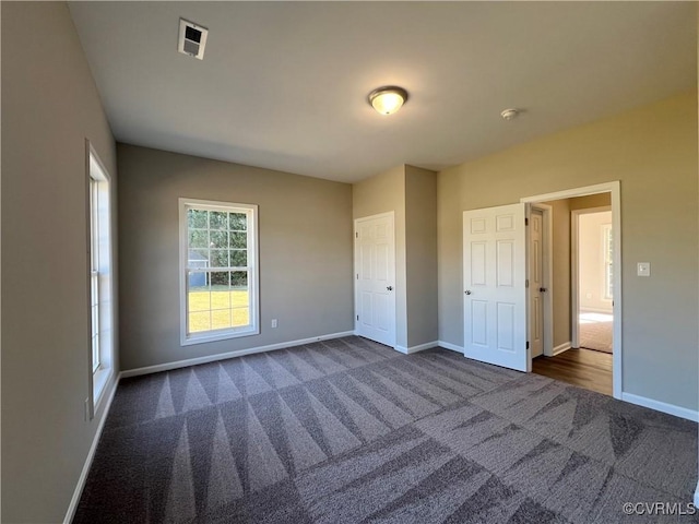 unfurnished bedroom with visible vents, dark carpet, and baseboards