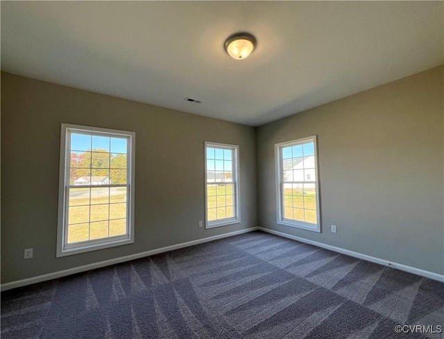 spare room with baseboards, visible vents, and dark colored carpet