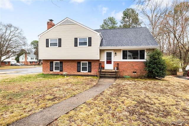 tri-level home featuring a shingled roof, a front yard, brick siding, and a chimney