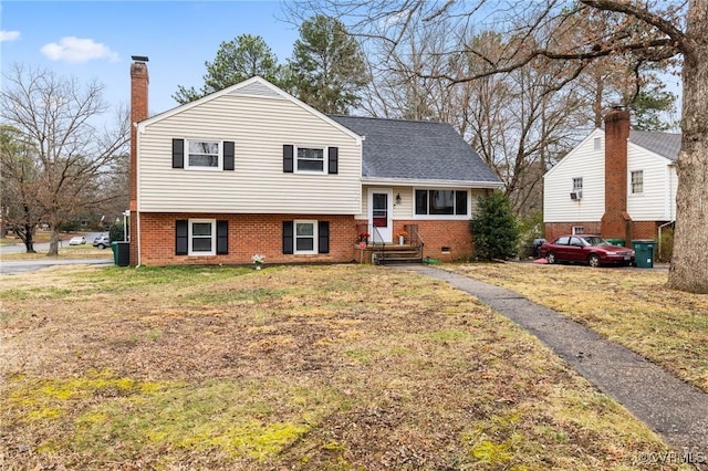 split level home with brick siding, a chimney, a shingled roof, cooling unit, and a front lawn