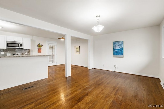 unfurnished living room featuring a sink, baseboards, visible vents, and dark wood-type flooring