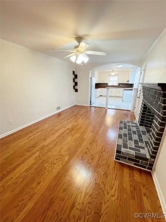 unfurnished living room with a tile fireplace, wood finished floors, visible vents, a ceiling fan, and baseboards