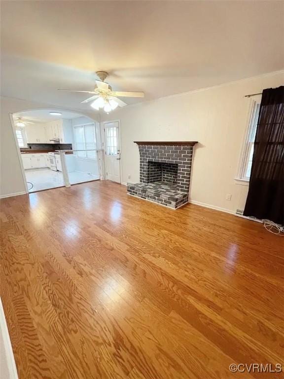 unfurnished living room featuring a ceiling fan, a brick fireplace, baseboards, and wood finished floors