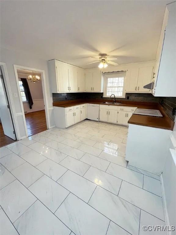 kitchen featuring dark countertops, backsplash, white cabinets, a sink, and ceiling fan with notable chandelier