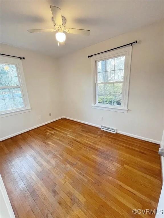 unfurnished room with baseboards, wood-type flooring, visible vents, and a healthy amount of sunlight