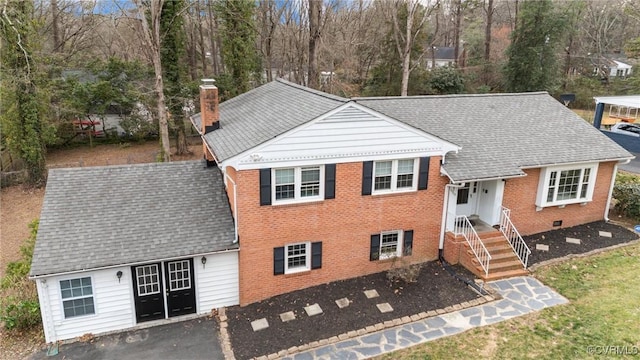 split level home with brick siding, a chimney, and roof with shingles