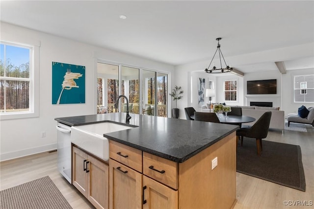 kitchen featuring a fireplace, light wood finished floors, open floor plan, a kitchen island with sink, and a sink