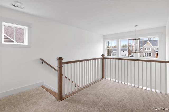 hall with carpet flooring, a notable chandelier, visible vents, and baseboards