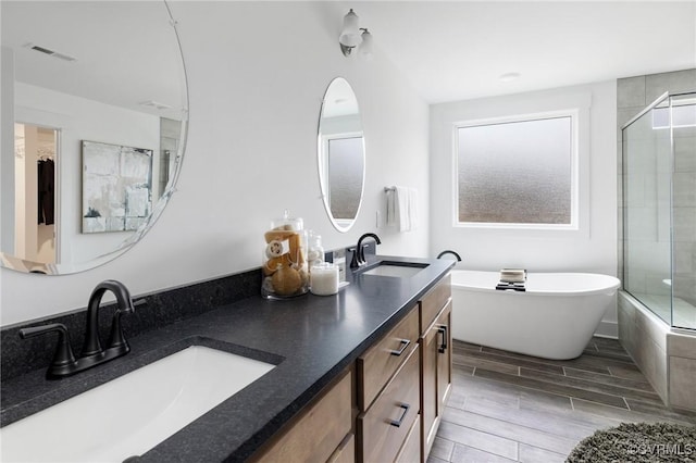 full bath with wood tiled floor, a freestanding tub, visible vents, and a sink