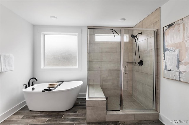 full bath with wood finish floors, a stall shower, a soaking tub, and baseboards