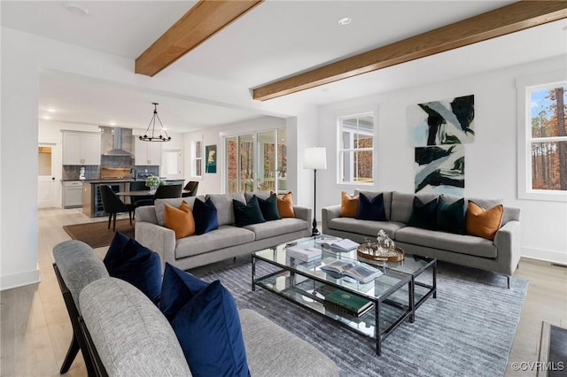 living area with a chandelier, light wood-style flooring, beverage cooler, baseboards, and beam ceiling