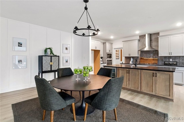 dining room with light wood-style floors, recessed lighting, a decorative wall, and an inviting chandelier