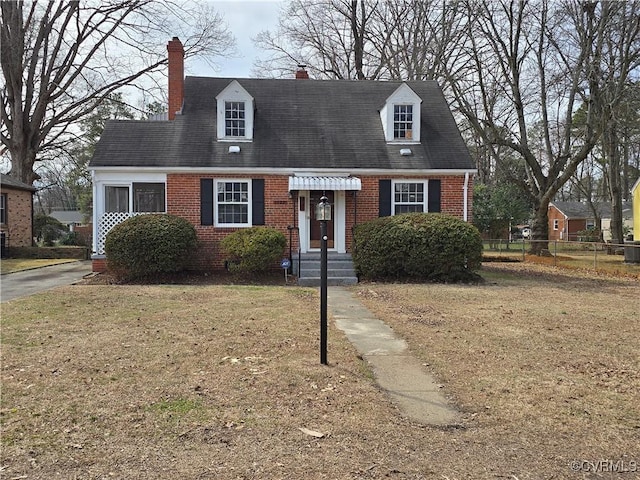 cape cod home featuring brick siding, a front lawn, a chimney, and fence