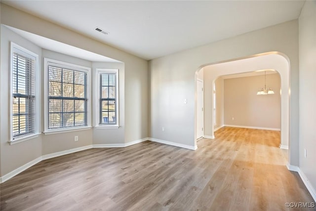 unfurnished room with plenty of natural light, visible vents, arched walkways, and a notable chandelier