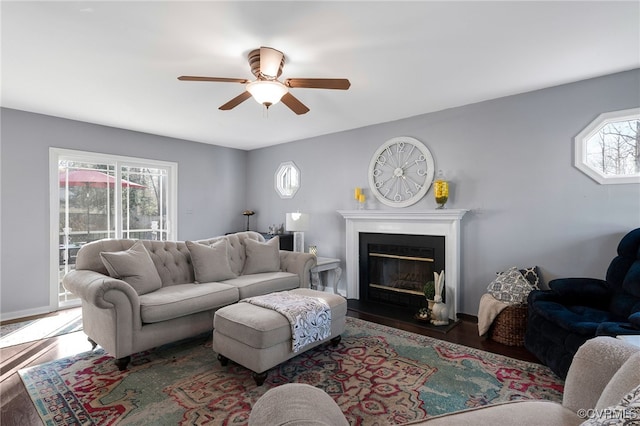 living area featuring a healthy amount of sunlight, a ceiling fan, wood finished floors, and a glass covered fireplace