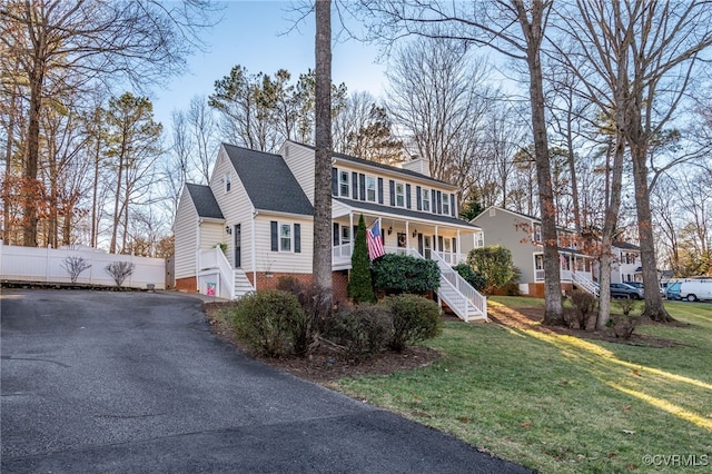 view of front of home featuring a chimney, covered porch, driveway, a front lawn, and stairs