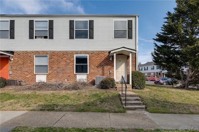 view of front of property with a front yard, cooling unit, and brick siding