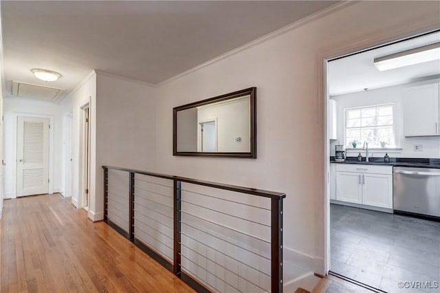 corridor with wood finished floors, a sink, an upstairs landing, baseboards, and ornamental molding